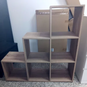 Stufen-Regal in Eiche Nachbildung. Unterste Ebene mit 3 quadratischen Abteilen, mittlere Ebene mit 2 quadratischen Abteilen, oberste Ebene mit einem quadratischen Abteil. Die rechte Regalseite ist über die ganze Höhe gerade, nach links fallen die "Stufen" ab.